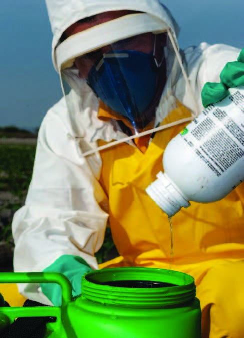 A photo of a pesticide applicator wearing personal protective equipment while mixing pesticide. 