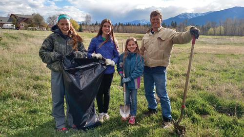 A family is dressed to work outside and standing with a shovel and plastic bag for cleanup. 