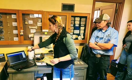 A woman (Sarah Maninger) pointing to lab equipment. Photo by Brent Roeder. 