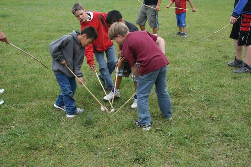 Four boys reach their double ball sticks toward the ground to gain control of the double ball. 