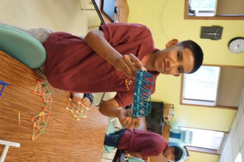 Photo of Micah Falls Down with a 3D printed plastic bridge with gumdrop and toothpick samples on the table. Taken by Jodie DeLay.
