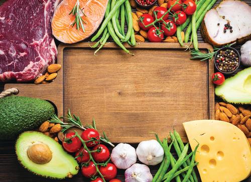 Cutting board with garlic, tomatoes and other vegetables and food next to it. 
