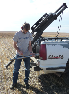 A large black truck-mounted soil probe with a soil scientist in front of it